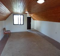 2 budovy v centre Komárna na predaj! - Podkrovná miestnosť v rodinnom dome s dreveným stropom a jednoduchým nábytkom.