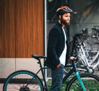 DOWNTOWN YARDS - 3i byt do vnútrobloku, blok A - Muž s bicyklom a prilbou na pozadí moderného bicyklového parkovania.