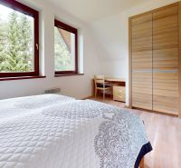 Pripravujeme do ponuky jedinečný apartmánový bytový dom Donovaly  - Spálňa v Chate s podlahou s dreveným dekorom, posteľou a výhľadom na stromy.