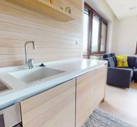 Pripravujeme do ponuky jedinečný apartmánový bytový dom Donovaly  - Interiér chaty s kuchynskou linkou, pohovkou a podlahou s dreveným dekorom.