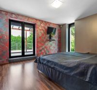 ARCHITEKTÚRA TICHA A MODERNÝCH TECHNOLÓGIÍ - SMART VILLA V OBJATÍ LESA - Spálňa v rodinnom dome s posteľou, farebnými stenami a podlahou s dreveným dekorom.