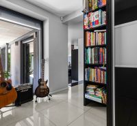ARCHITEKTÚRA TICHA A MODERNÝCH TECHNOLÓGIÍ - SMART VILLA V OBJATÍ LESA - Interiér rodinného domu, knihy, dve gitary a zosilňovač na podlahe s dlažbou.