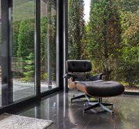 ARCHITEKTÚRA TICHA A MODERNÝCH TECHNOLÓGIÍ - SMART VILLA V OBJATÍ LESA - Kožené kreslo pri veľkých preskleniach s výhľadom na zeleň v rodinnom dome.
