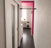REZERVOVANÝ - Na predaj priestranný 2-izbový byt s balkónom, klímou... - Chodba 2-izbového bytu s posuvnými dverami, podlaha s dreveným dekorom, ružová stena.