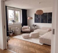 Priestranný 3-izbový byt | 72 m² + 9 m² loggia + 9 m² pivnica |  - Obývacia izba v 3-izbovom byte s pohovkou, kreslom a podlahou s dreveným dekorom.