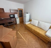 Garsonka Topoľčany / PRENAJOM - Garsónka s podlahou s dreveným dekorom, kuchynský kút a žltá pohovka.