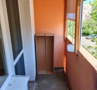 Pekný 1 izbový byt s balkónom na prenájom - Balkón 1-izbového bytu, oranžová stena, drevená skrinka, výhľad na stromy a cestu.