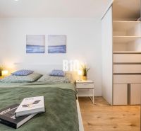 VILA ĽADOVÁ | MODERNÝ 2IZBOVÝ BYT V KOMORNOM PROJEKTE PRI RAČIANSKOM M - Spálňa v 2-izbovom byte s posteľou, skriňou a podlahou s dreveným dekorom.