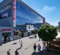 Obchodné priestory s charakterom v srdci Topoľčian – investícia, ktorá - Obchodné priestory na Obchodnej ulici v Topoľčanoch, ľudia prechádzajú popri moderných budovách.