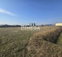 NA PREDAJ EXKLUZÍVNE: Lukratívny pozemok 6 086m2 – Hriadky (okres TV)  - Tráva a výrobné priestory v Hriadkach pod jasnou oblohou, s priemyselnou budovou na obzore.