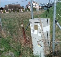 Pozemok v Dunajskej Lužnej  - Plot s trávou a elektrickým rozvádzačom na pozemku na bývanie v Dunajskej Lužnej.