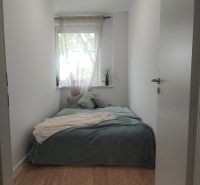 Novozrekonštruovaný 4-izb. byt, Exnárova ul., Ružinov - Pošeň - Úzka spálňa s posteľou a oknom, podlaha s dreveným dekorom, svetlý interiér.