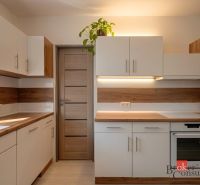 Priestranný 4i byt s parkovacím miestom 20min od Bratislavy - Kuchyňa s podlahou s dreveným dekorom, bielo-hnedé skrinky, rastlina na skrinke.