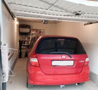 Garáž na prenájom- Staré mesto- Belanská, automatická brána - Červené auto zaparkované v garáži s regálmi na stene, podlaha z dlažby.