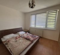 Na prenájom útulný 1,5-izbový byt na Okružnej ulici - Spálňa v 2-izbovom byte s posteľou, vedľa okna so žalúziami a skriňou.