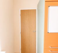 Predaj! slnečný 3-izbový byt s loggiou 74 m² Podbreziny - LM - Dvere a oranžová kuchynská linka v 3-izbovom byte s podlahou s dreveným dekorom.