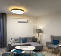 Nové skolaudované byty a apartmány vo Vajnoroch. - Obývacia izba v 2-izbovom byte s podlahou s dreveným dekorom a sivými sedačkami.