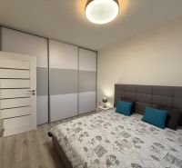 Nové skolaudované byty a apartmány v projekte Diamant. - Spálňa v 2-izbovom byte s posteľou, šatníkovou skriňou a podlahou s dreveným dekorom.