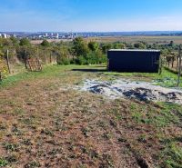 Oplotený obrábaný vinohrad so studňou.Fajgalská cesta - Výhľad z Rekreačných pozemkov na Fajgalskej ceste v Pezinku s trávnatou plochou a záhradným domčekom.