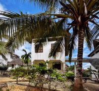 SAMOSTATNE STOJACA VILA MAPUMZIKO S 2 IZBAMI NA ZANZIBARE  - Rodinný dom v Pwani Mchangani obklopený palmami a kvetmi na kamennej terase.