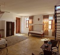 SAMOSTATNE STOJACA VILA MAPUMZIKO S 2 IZBAMI NA ZANZIBARE  - Priestranná izba s posteľou, stoličkami a rebríkom v rodinnom dome.