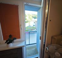 PREDAJ 2-izbový byt Harmanec 56 m2 s balkónom  - Balkónový výhľad z 2-izbového bytu s rastlinou a ventilátorom pri okne.