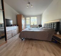 3 izbový byt s balkónom Topoľčany  - Spálňa v 3-izbovom byte s posteľou, šatníkovou skriňou a podlahou s dreveným dekorom.