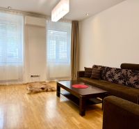 Na prenájom 2 izbový byt, 65 m2, Bratislava, centrum, Vajanského nábr. - Obývacia izba s drevenou podlahou a hnedou sedačkou v 2-izbovom byte.