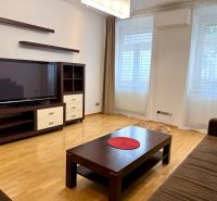 Na prenájom 2 izbový byt, 65 m2, Bratislava, centrum, Vajanského nábr. - Obývacia izba v 2-izbovom byte s pohovkou, televízorom a dreveným nábytkom.