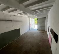 Ponúkame na predaj garáž, Vyhnianska cesta, Bratislava - Nové Mesto. - Interiér garáže s betónovou podlahou a otvorenými plechovými dverami.