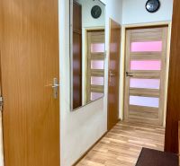 Na predaj 2 izbový byt, 47 m2, Bratislava, Nové Mesto, Piešťanská ul. - Chodba s podlahou s dreveným dekorom v 2-izbovom byte, zrkadlo a hodiny na stene.