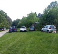 Rekreačná chata s výhľadom na Líščie údolie a Yuventu, Karlová Ves - Autá parkujúce na tráve pri ceste medzi stromami v oblasti Karloveská, Bratislava - Karlova Ves.