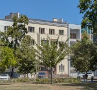 Výnimočné bývanie - Mezonet v úplnom centre Nitry  - Budova na ulici Kúpeľná v Nitre, obklopená stromami a zaparkovanými autami.