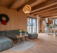 I Luxusné dvojpodlažné chalet pri Liptovskej Mare - Svetlá obývacia izba s kuchyňou, sedačkou, stolom a podlahou s dreveným dekorom.