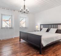 Stavebný pozemok 8 500 m² s podnikateľským potenciálom - Spálňa s posteľou, podlahu zdobí drevený dekor, svetelný luster, záclony na oknách.