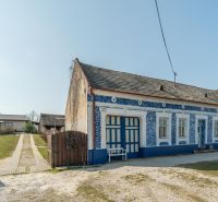 Stavebný pozemok 8 500 m² s podnikateľským potenciálom - Tradičný modrobiely dom na bývanie v Dolnom Lopašove, obklopený zelenými pozemkami.