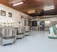 I PREDAJ – FUNGUJÚCA PEKÁREŇ A POTRAVINY V TRNAVE - Priemyselná kuchyňa s nerezovými nádobami, kuchynským zariadením a obkladom na stenách.