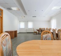 I PREDAJ – FUNGUJÚCA PEKÁREŇ A POTRAVINY V TRNAVE - Priestranná miestnosť s drevenými stolmi a stoličkami, neutrálna farebná paleta.