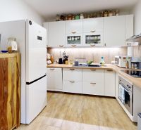 Rodinný dom 240 m², 3 bytové jednotky, veľký pozemok, Lamač - Kuchyňa v rodinnom dome s podlahou s dreveným dekorom, biele skrinky, kuchynské spotrebiče.
