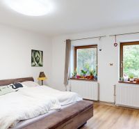 Rodinný dom 240 m², 3 bytové jednotky, veľký pozemok, Lamač - Spálňa rodinného domu s manželskou posteľou, dreveným dekorom podlahy a rastlinami na parapete.