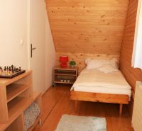Chalupa Tále, okr.Brezno, pozemok 680m2,  - Jednolôžková izba s podlahou s dreveným dekorom, šachovnicou na stolíku a oknom s bielou záclonou.