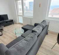 Pekný 2i byt, NOVOSTAVBA, PARKING, BALKÓN, KLÍMA, Jégého alej III. - Obývačka 2-izbového bytu s pohovkou, kreslom a TV, podlaha s dreveným dekorom.