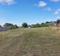 Stavebný pozemok 1 750 m² v centre obce Rumanová - Pozemok na bývanie v Rumanovej, tráva, plot, záhrada, jasná obloha.