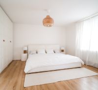 Dom medzi stromami: Nadčasová architektúra v Cabaj-Čápore - Svetlá spálňa s bielou posteľou a podlahou s dreveným dekorom v rodinnom dome.