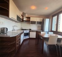 NOVINKA!!! Priestranný 3-izbový byt, 72 m² | Karpatská, Sásová - Kuchyňa v 3-izbovom byte s podlahou s dreveným dekorom a jedálenským stolom.