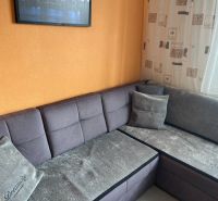 NA PREDAJ PRIESTRANNÝ 3-IZBOVÝ BYT | 67 m² | LODŽIA | 4. POSCHODIE - Šedá sedačka v rohu obývačky v 3-izbovom byte s oranžovou stenou.