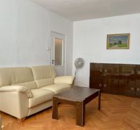 I PREDAJ 2-IZBOVÝ BYT S KLIMATIZÁCIOU A BALKÓNOM I RUŽINOV - Obývacia izba s krémovou sedačkou, dreveným stolíkom a skrinkou na podlahe s dreveným dekorom.