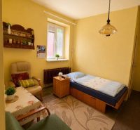 NA PREDAJ - Rodinný dom - Banská Bystrica - CENTRUM - Izba v rodinnom dome: posteľ, kreslá, stolík, koberec a okno so žaluziami.