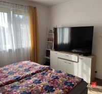 Predaj bungalovu - drevodom - Spálňa v rodinnom dome s TV, kvetinové obliečky, žlté závesy, okno.