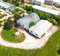 Skladový areál s pozemkom 10 000 m2 v priemyselnej zóne - Priemyselné haly a sklady obklopené zeleňou v Senici, ukazujúci rozľahlé betónové plochy.